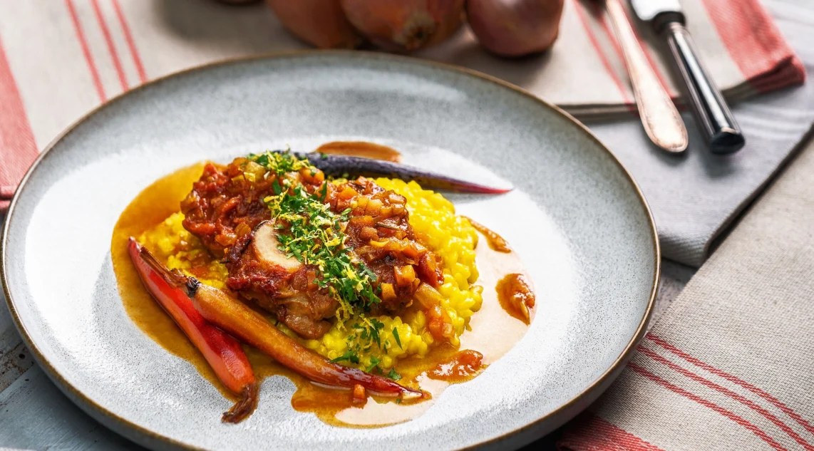Ossobuco alla Milanese mit Safranrisotto und glasierten Möhren serviert auf einem grauen Steinzeugteller