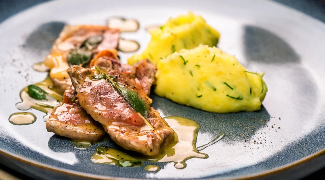 Saltimbocca Romana serviert mit Kartoffelpüree auf einem blauen Teller.