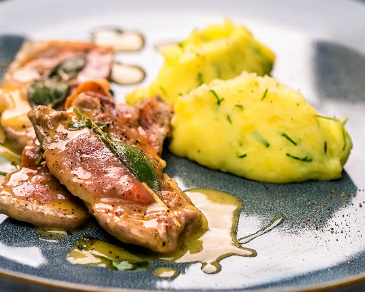 Saltimbocca Romana serviert mit Kartoffelpüree auf einem blauen Teller.