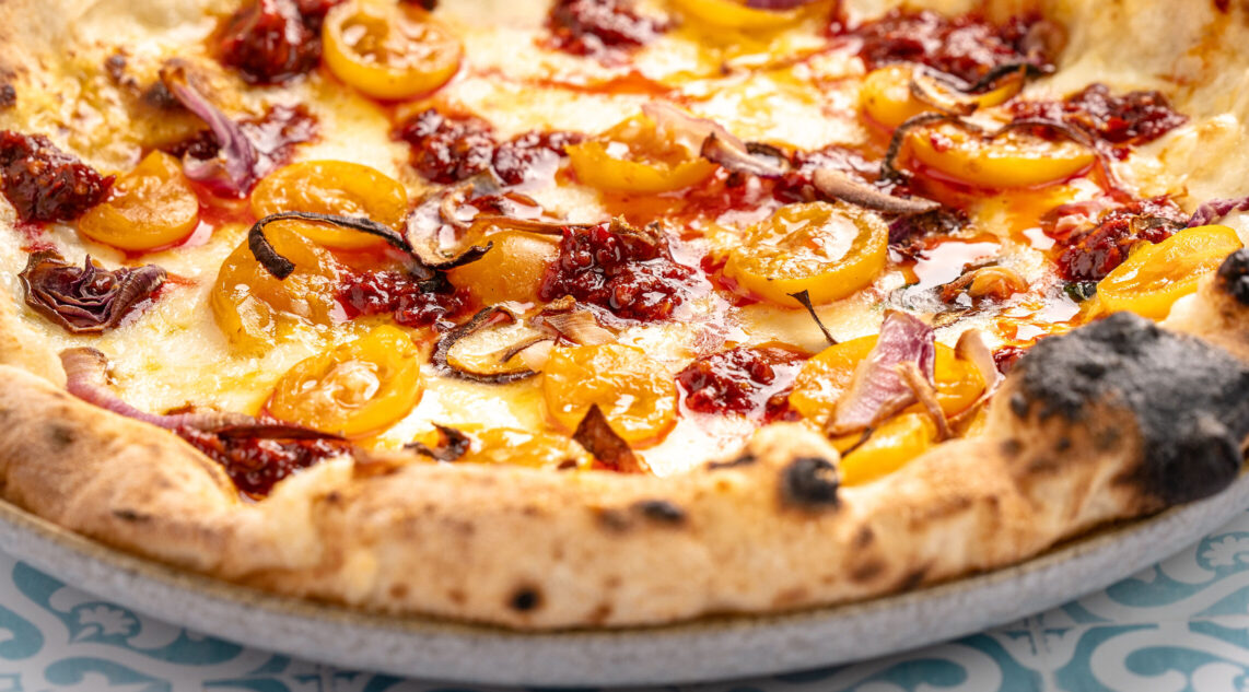 die saftige Oberseite einer neapolitanischen Pizza belegt mit Nduja, gelben Tomaten und Fior di Latte ist zu sehen