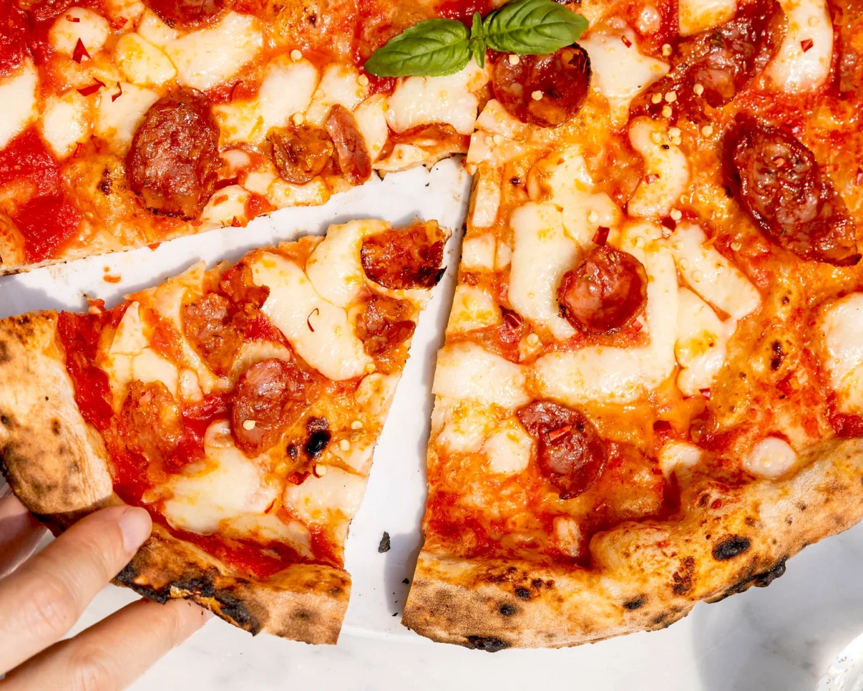 Nahaufnahme einer Hand, die ein Stück frisch gebackener Pizza Diavola nimmt