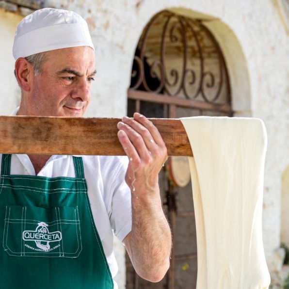 ein Käsehersteller zieht den Mozzarella mit einem Holzwerkzeug lang, Handarbeit in Italien