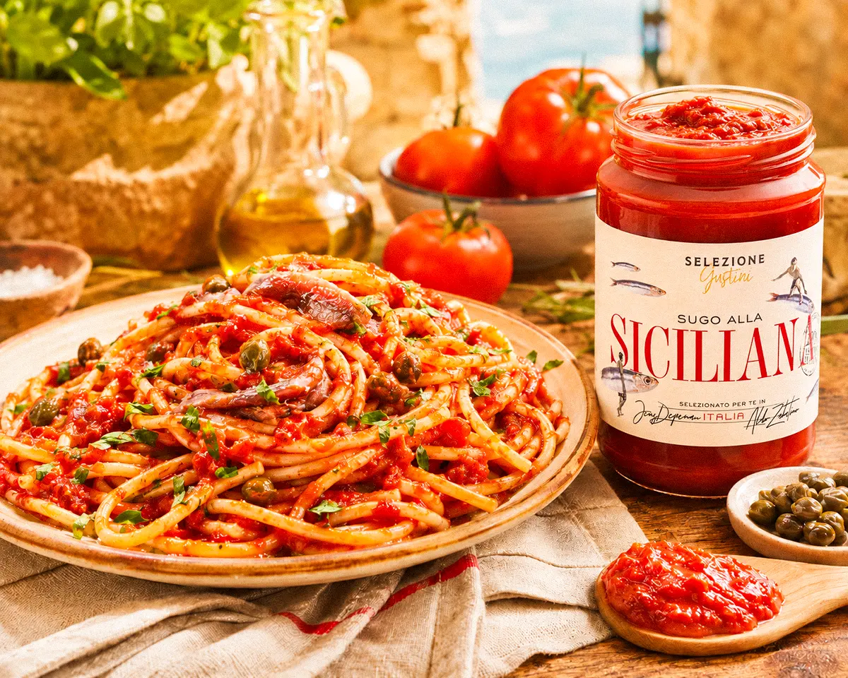 Spaghetti mit würzigem Tomatensugo, Sardellen, Kapern und Oliven neben einem Glas Sugo alla Siciliana.