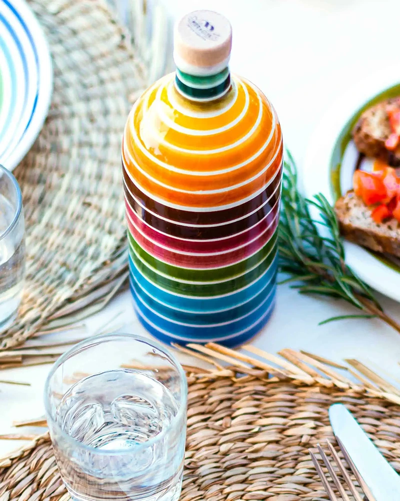 Muraglia Olivenöl - Regenbogen Keramikflasche – Flasche im Hintergrund, in bunter Keramikflasche präsentiert