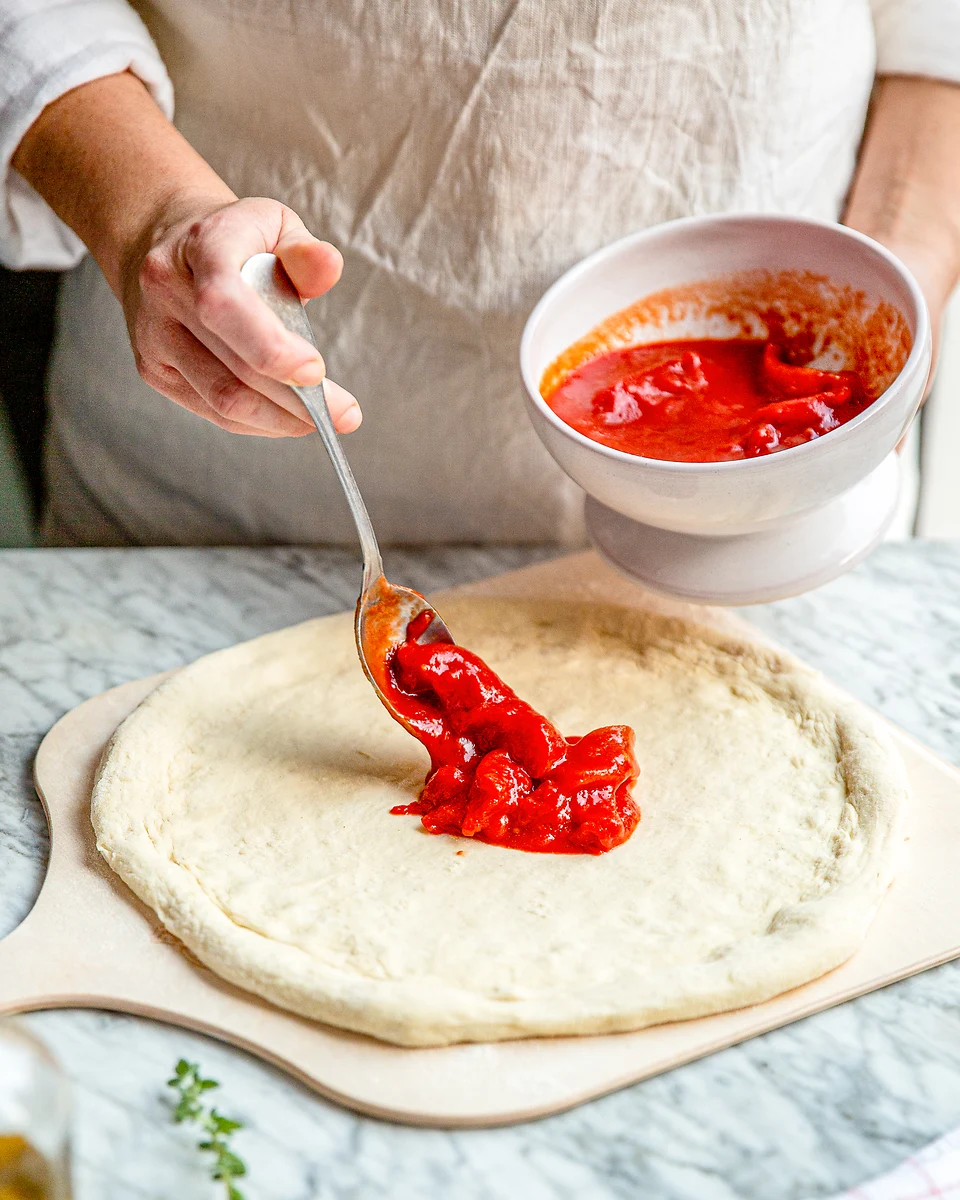 Rohe San-Marzano-Tomatensauce wird auf Pizzateig verteilt