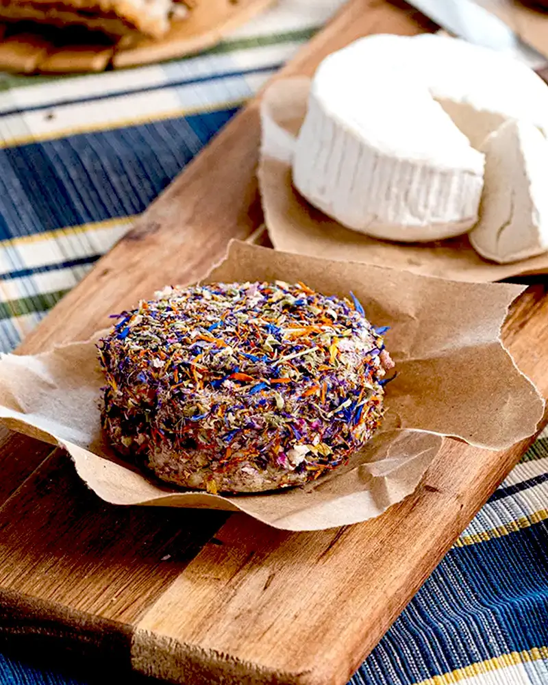 veganer Käse mit Blütenmantel liegt auf einem Holzbrettchen, Fiori Eduli